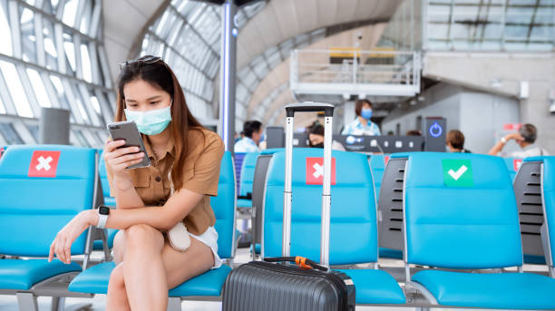 Asian woman wearing a mask sits in the terminal at the airport. New normal in air travel.