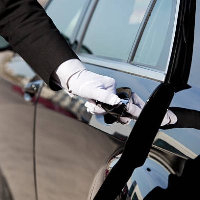 The white gloved hand of a uniformed chauffeur / doorman opening / closing a luxury car door.